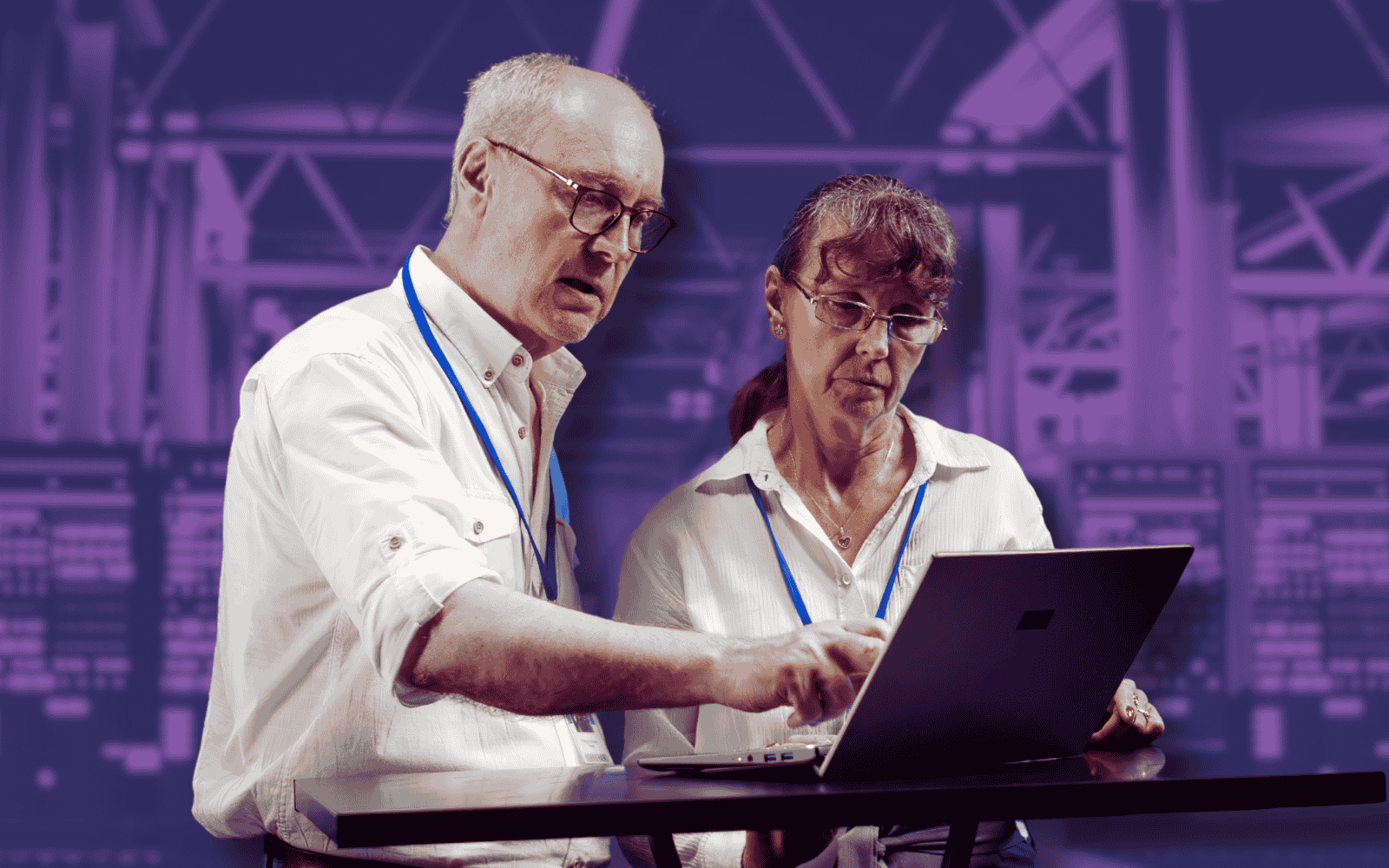 Two technicians wearing ID badges collaborate on a laptop in front of a blurred server room background. This image could represent the collaborative nature of managing public cloud computing resources.