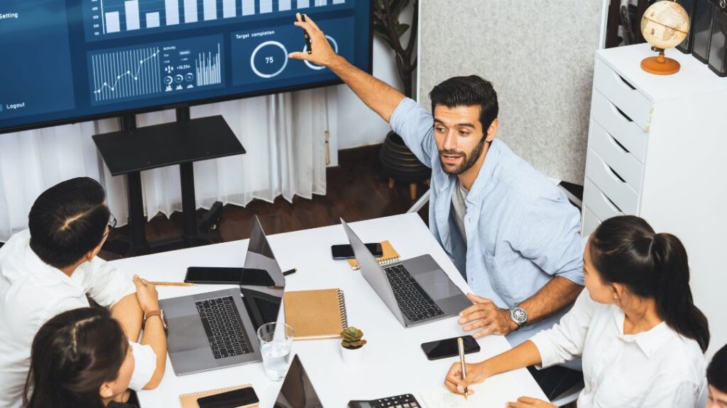 Team meeting with professional presenting BI dashboard on screen showing analytics and KPIs, demonstrating measuring BI success for real business impact.