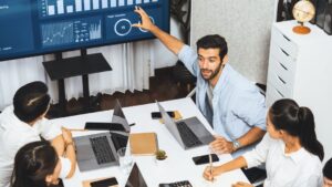 Team meeting with professional presenting BI dashboard on screen showing analytics and KPIs, demonstrating measuring BI success for real business impact.